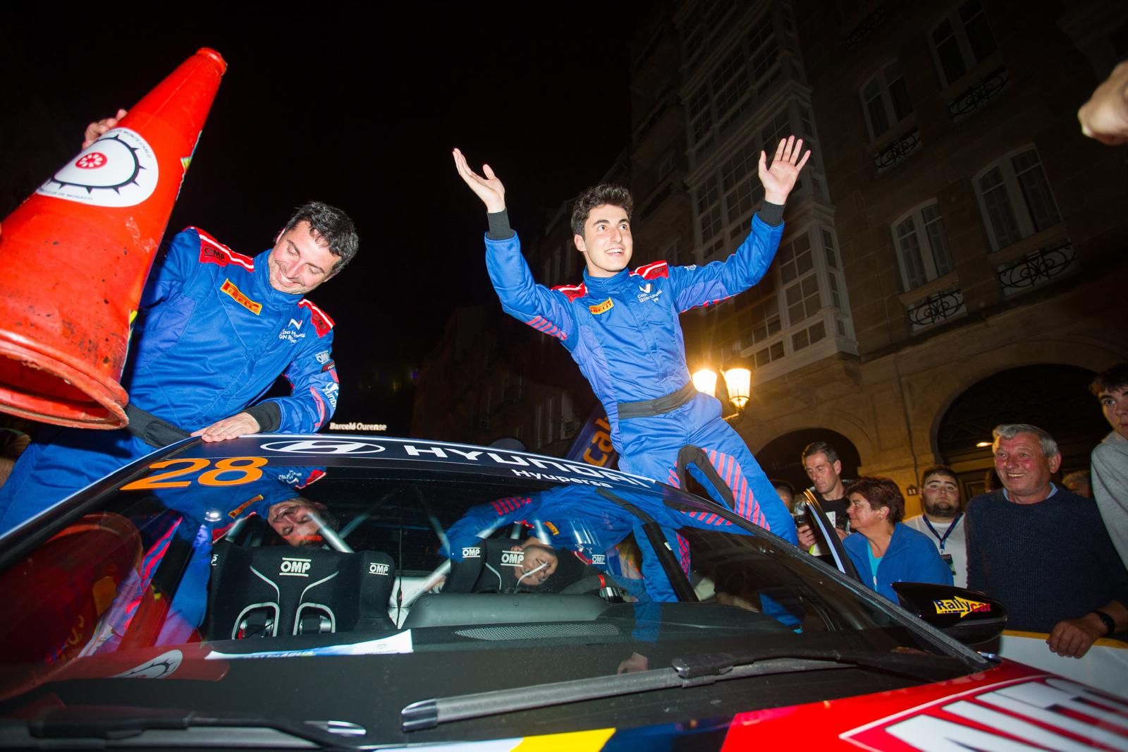 Alejandro Medín celebrando subido al Hyundai i20N junto a su copiloto ante la afición, de noche