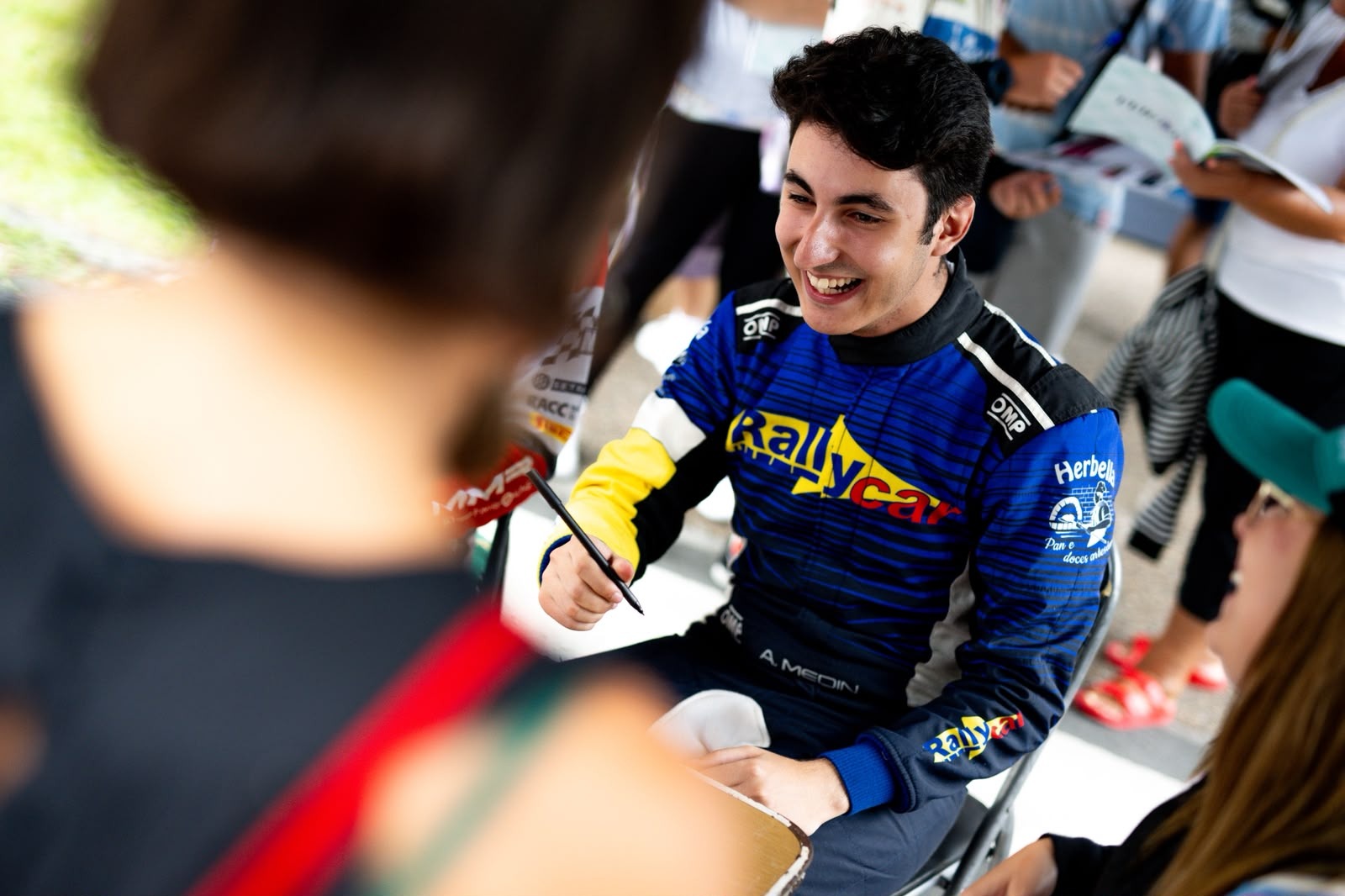 Alejandro Medín sonriendo con el mono de Rallycar mientras firma autógrafos a los aficionados